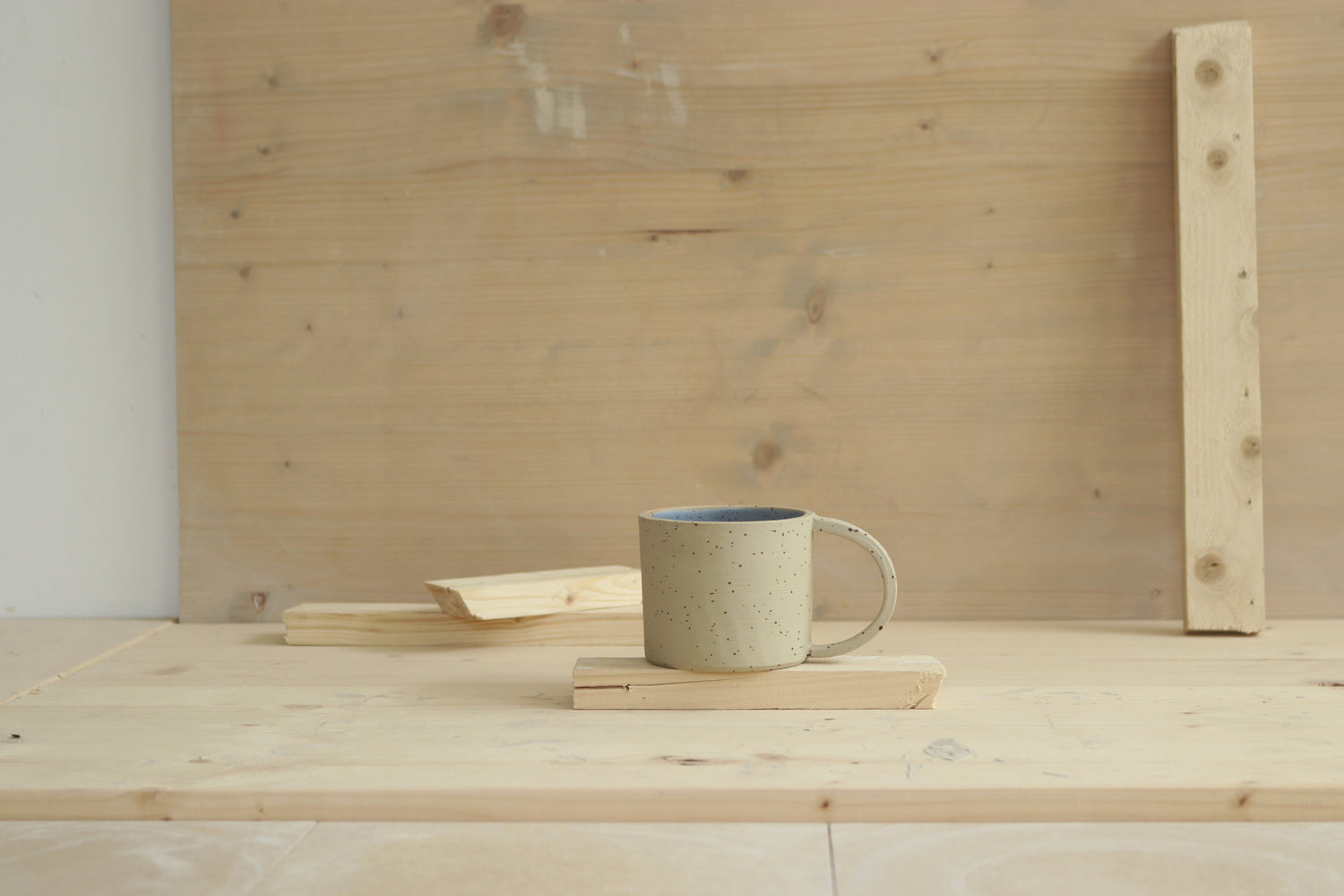 Handmade speckled stoneware ceramic mug with a wide-grip D handle, raw, unglazed clay exterior and a soft blue glazed interior